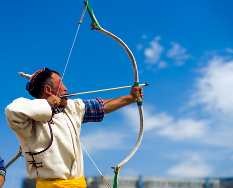 Ulaanbaatar, Mongolia - June 11, 2007: A traditionally dressed man archer taking aim with his bow and arrow at the Naadam Festival archery competition held at an open public field with free admission
