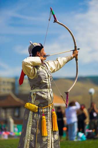Ulaanbaatar, Mongolia - June 11, 2007: A beautifully dressed Mongolian woman archer aiming her arrow at the traditional Naadam Festival female archery competition held at an open public field with free admission