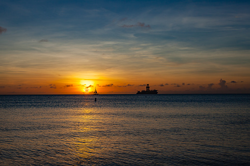 The sun sets off the West Coast of Aruba in the Caribbean Sea. It turns to horizon into gold. A sailing ship can be seen on the horizon as well as an Oil drilling Rig. Photo shot in the late afternoon sunlight. Camera: Canon EOS 5D MII. Lens: Canon EF 24-70 mm F2.8L USM