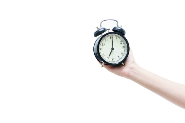 istock Woman's hand holding black traditional wind-up (keywound), mechanical, spring-driven alarm clock isolated on white background 853110330
