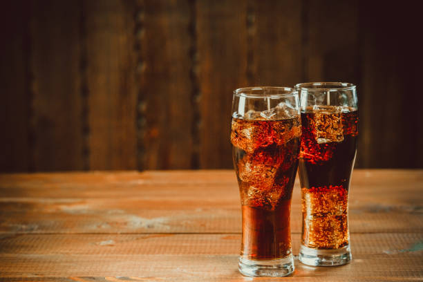 Beautiful cold fizzy cola soda with cubes ice in glasses goblet on old wooden background with free space. Shallow DOF. stock photo