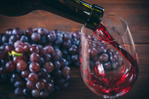 Pouring red wine into the glass with a bunch of red grapes against wooden background stock photo