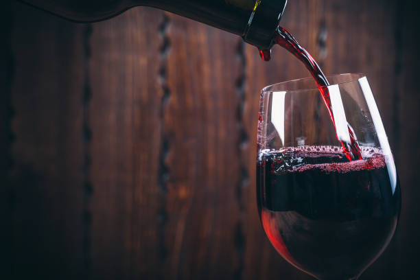 Pouring red wine into the glass against wooden background stock photo