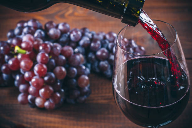 Pouring red wine into the glass with a bunch of red grapes against wooden background stock photo