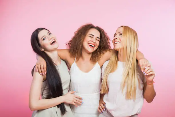 Three young women laughing and having fun together. Girlfriends hugging and smiling happily. Female company of best friends. Blonde curly brown and long dark hair.