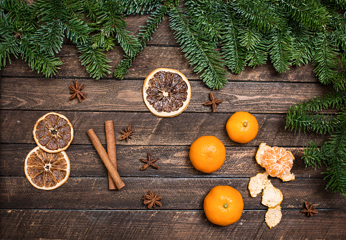 Christmas decor with tangerines, dried orange slices, anise, cinnamon sticks, branch of spruce on a wooden surface.