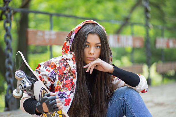 skater, adolescente con pattino. la testa del ritratto ravvicinato ha sparato alla bella giovane donna bruna che tiene il pattino seduto su uno sfondo di ponte legnoso. concetto di vita di espressione facciale dell'emozione umana positiva - headshot human face head and shoulders latin american and hispanic ethnicity foto e immagini stock