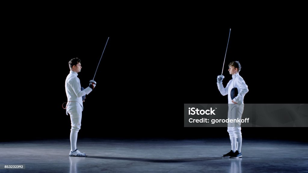 Two Young Professional Fencers Greet Each Other, and Preparing for Fighting Match. Shot Isolated on Black Background. Boys Stock Photo
