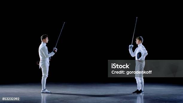 Two Young Professional Fencers Greet Each Other And Preparing For Fighting Match Shot Isolated On Black Background Stock Photo - Download Image Now