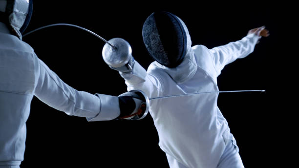 dos profesional tiradores show magistral manejo de la espada en su lucha contra el papel. atacar, defender, salto y empuje y arremeter. disparo aislado sobre fondo negro. - fencing sport athlete sword fotografías e imágenes de stock