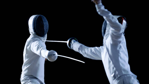 Two Professional Fencers Show Masterful Swordsmanship in their Foil Fight. They Attack, Defend, Leap and Thrust and Lunge. Shot Isolated on Black Background. Two Professional Fencers Show Masterful Swordsmanship in their Foil Fight. They Attack, Defend, Leap and Thrust and Lunge. Shot Isolated on Black Background. fleche stock pictures, royalty-free photos & images