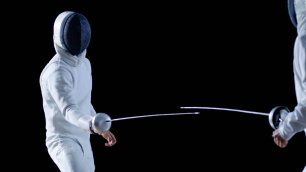 istock Two Professional Fencers Show Masterful Swordsmanship in their Foil Fight. They Attack, Defend, Leap and Thrust and Lunge. Shot Isolated on Black Background. 853233602