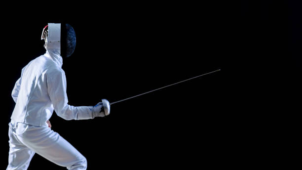 Side View of a Fully Equipped Skilled Fencer Training His Attack and Lunge with a Foil. Shot Isolated on Black Background. Side View of a Fully Equipped Skilled Fencer Training His Attack and Lunge with a Foil. Shot Isolated on Black Background. fleche stock pictures, royalty-free photos & images