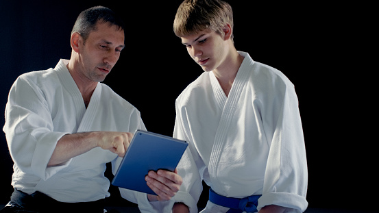 Martial Arts Master Wearing Hakamas Teaches Young Student Aikido Technique with the Help of the Tablet Computer. Shot Isolated on Black Background.