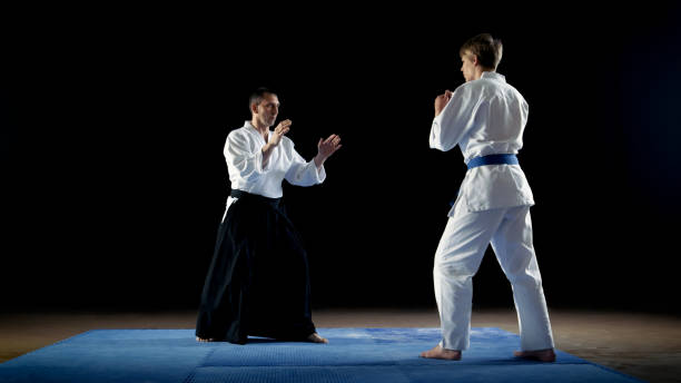 istock Martial Arts Master Wearing Traditional Samurai Hakamas Teaches Young Student Aikido Technique How To Reflect Fist Blows and Overpower Your Enemy. Shot Isolated on Black Background. 853236844