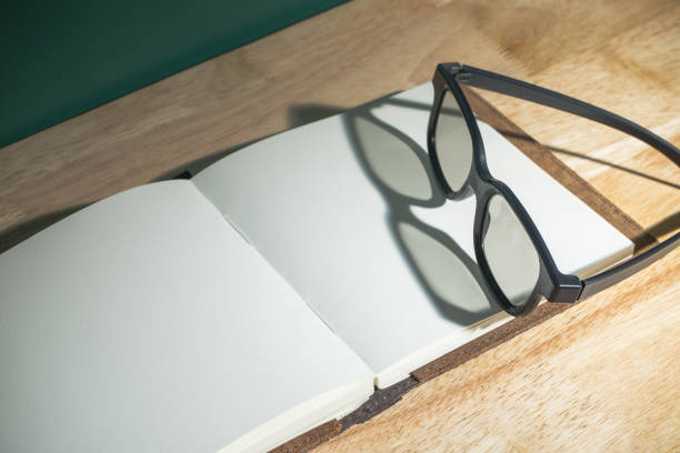 istock Close up black eyeglasses on open blank book with shadow light from window on wooden table top and blackboard wall,Education concept,study resting 853253388