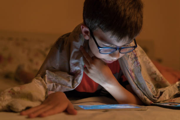 Boy Looking On Digital Tablet In Bed At Night Boy Looking On Digital Tablet In Bed At Night myopia photos stock pictures, royalty-free photos & images