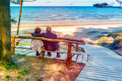 Happy elderly couple resting on the wooden bench of the Baltic Sea