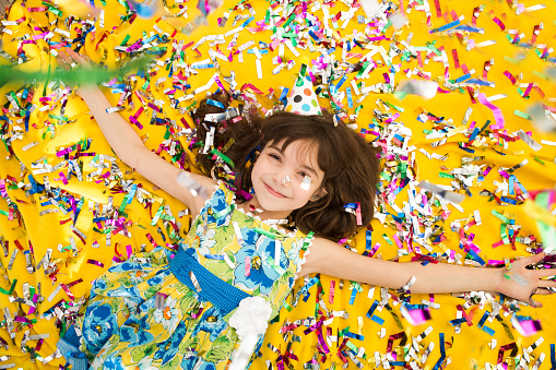 Happy kid celebrating party with blowing confetti top view. The girl in birthday party.  Positive emotions.