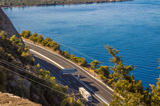 highway at the edge of ta cliff with trees on  the side and the blue ocean below