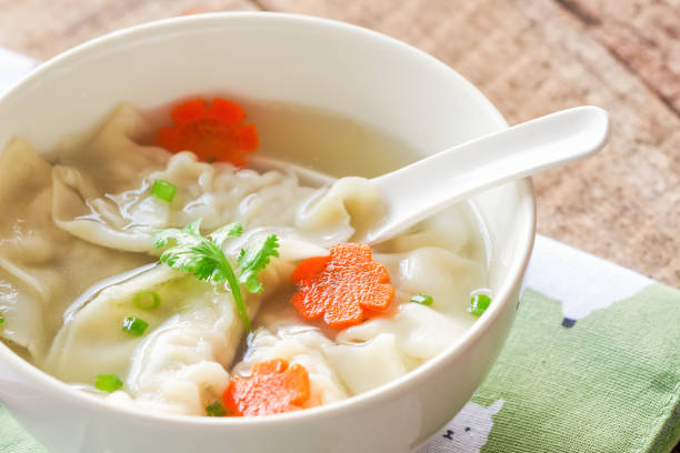 bouchent soupe wonton porc haché dans un bol blanc sur serviette mis sur la table en bois. maison wonton délicieux en soupe claire pour le petit déjeuner ou déjeuner ou dîner. soupe wonton est toujours populaire nourriture chinoise. - carrot close up silverware cutting board photos et images de collection