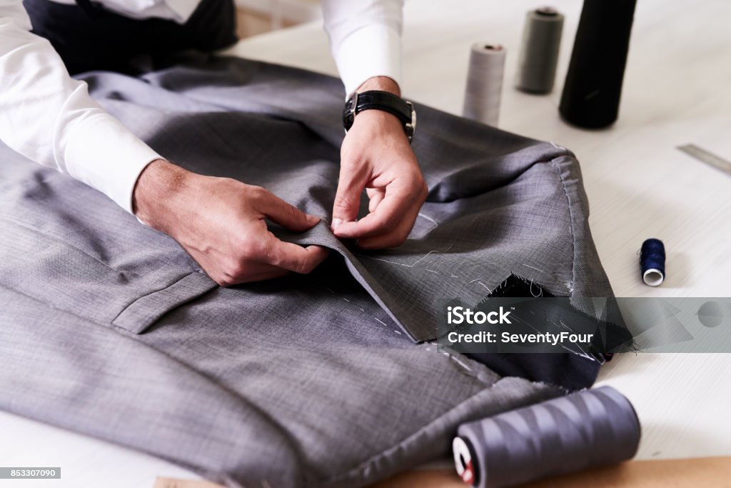 Creation of Stylish Male Jacket Production process of custom-made male jacket: unrecognizable tailor concentrated on sewing with needle and thread, close-up shot Textile Stock Photo