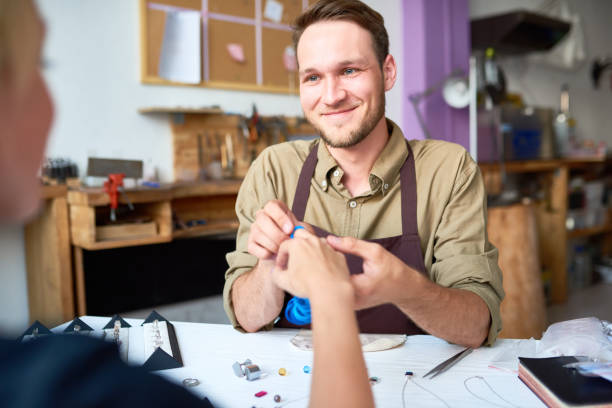 Portrait of smiling young man trying on ring sizes on clients hand in jewelry workshop