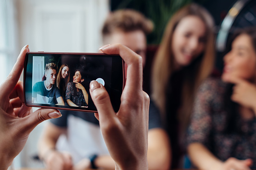 Mujer manos tomando la foto con el smartphone de jóvenes amigos alegres, fondo borroso photo