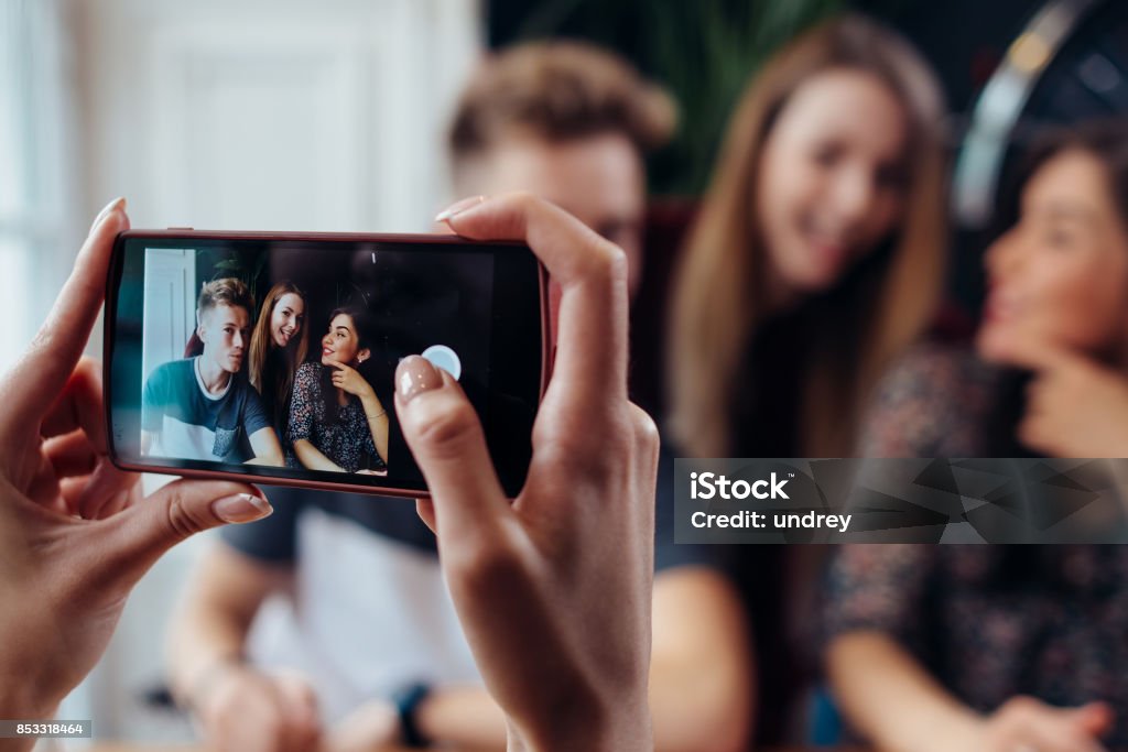 Mujer manos tomando la foto con el smartphone de jóvenes amigos alegres, fondo borroso - Foto de stock de Sacar una foto libre de derechos