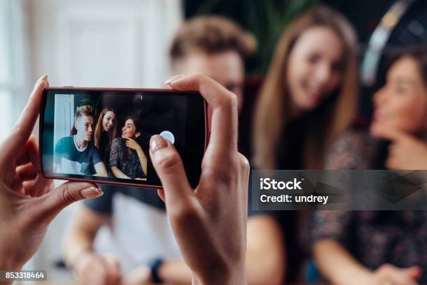 Female Hands Taking Photo With Smartphone Of Young Cheerful Friends Blurred Background Stock Photo - Download Image Now