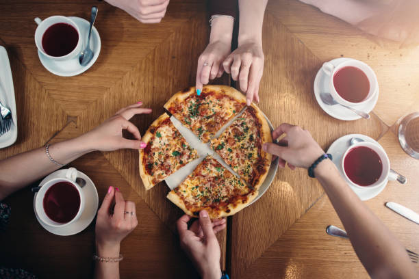 istock Top view of hands taking pizza slices from a plate standing on a table with tea cups around 853319008