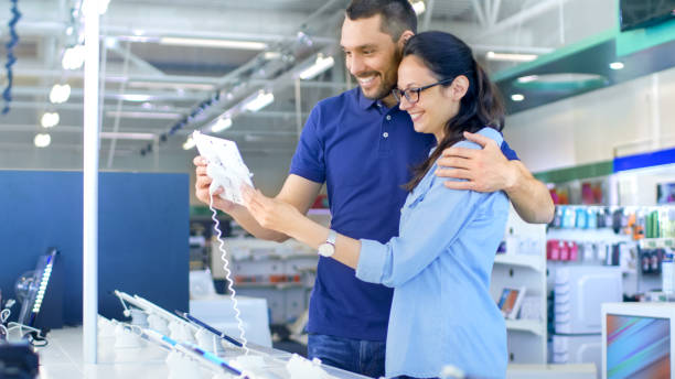 istock In the Electronics Store Beautiful Young Couple Looks at Latest Tablet Computer, They Think about Buying One. Store is Big, Bright and Has all the New Devices. 853324086