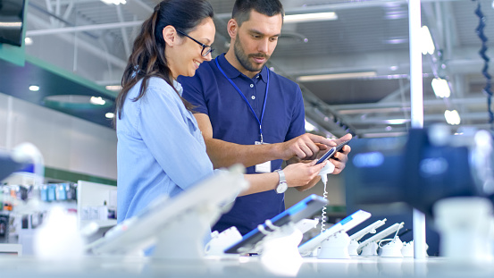 En el tienda de electrónica Consultor da asesoramiento profesional para una mujer joven, considera comprar la nueva tableta y necesita la opinión de los expertos. Tienda es moderno, luminoso y cuenta con todos los nuevos dispositivos. photo