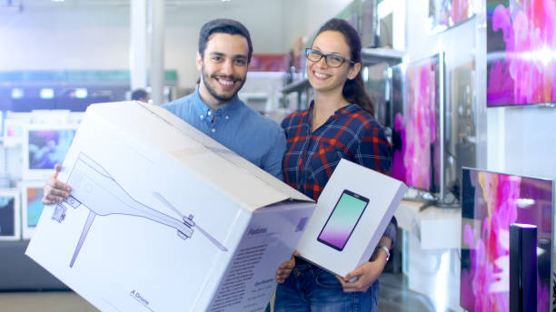 in the electronics store happy young couple poses with newly purchased drone and tablet computer. store is big and bright, has all the latest tv's, cameras and smartphones. - ipad shopping gift retail imagens e fotografias de stock