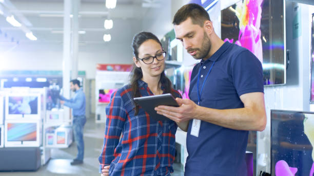 istock In the Electronics Store Professional Consultant Provides Expert Advice on Tablet Computer Specifications For Beautiful Young Woman. Store is Bright, Modern and Has all the Latest Devices. 853324160