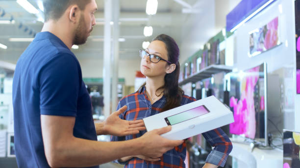 istock In the Electronics Store Professional Consultant Provides Expert Advice on Tablet Computer Specifications For Beautiful Young Woman. Store is Bright, Modern and Has all the Latest Devices. 853324232