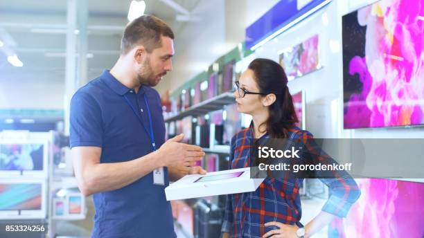 In The Electronics Store Professional Consultant Provides Expert Advice On Tablet Computer Specifications For Beautiful Young Woman Store Is Bright Modern And Has All The Latest Devices Stock Photo - Download Image Now