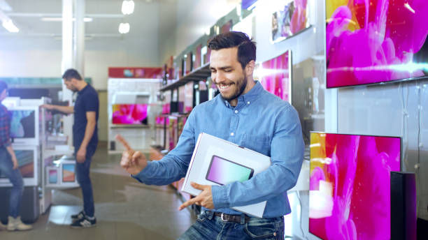 istock Young Man in Electronics Store Purchased Latest Model of the Tablet Computer and Dances Happily with the Box. Bright and Modern Store Has all the Latest Devices in Store. 853324290