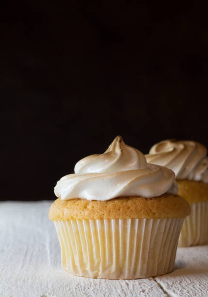 istock Cup cake with egg white meringue topping on white wooden table and one defocused against a dark bacground. 853325064