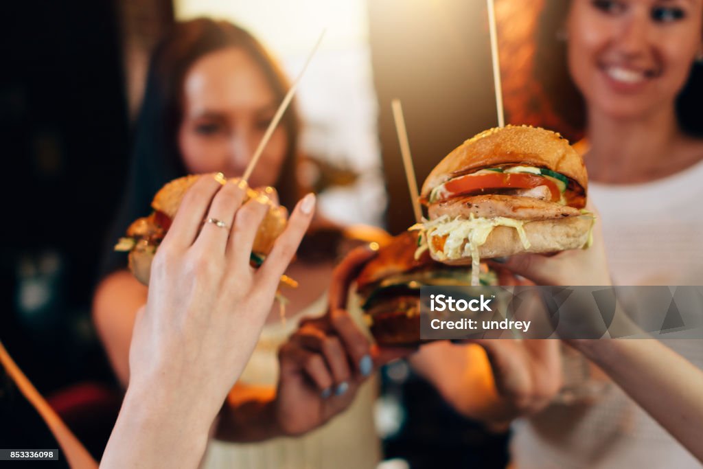 Femelle mains tenue gros hamburgers juteux savoureux avec des femmes floues à l’arrière-plan - Photo de Burger libre de droits