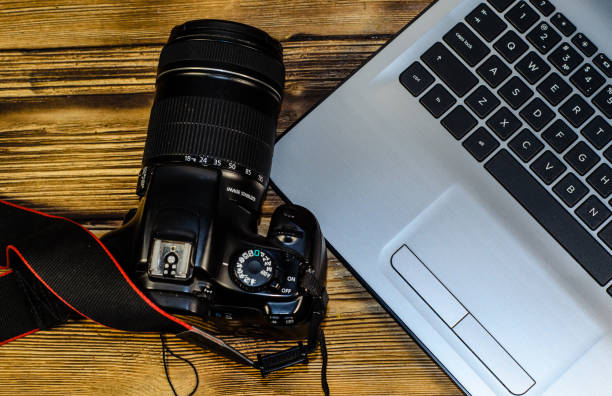 istock Modern DSLR camera and laptop on wooden table. Top view 853337636