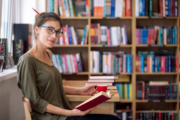 Woman with glasses reading a book with a cup of coffee stock photo