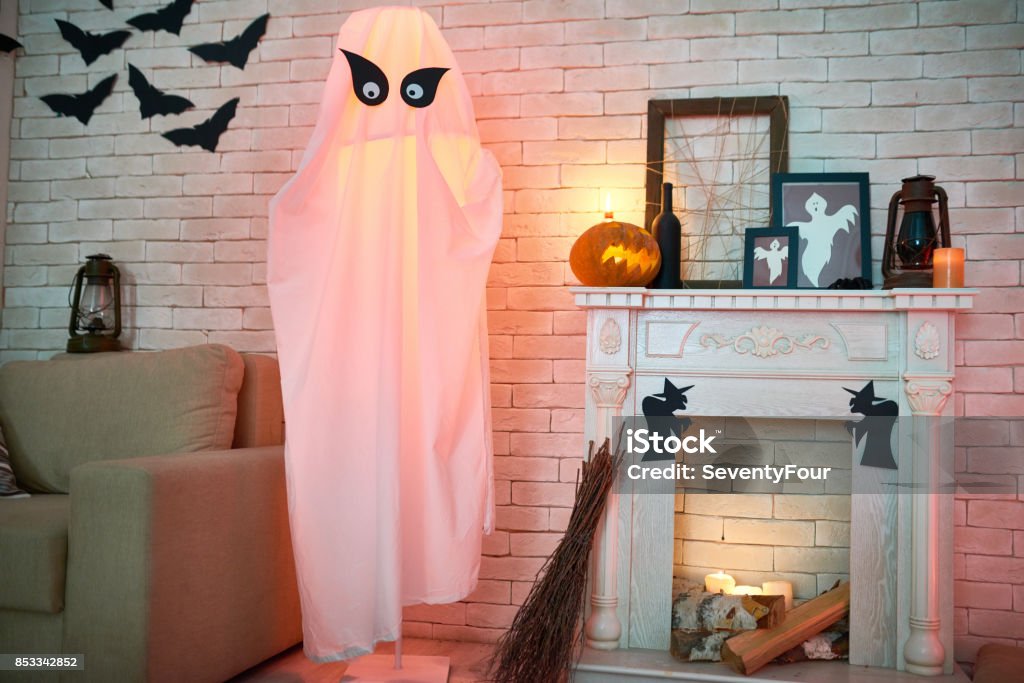 Mysterious room with Halloween decorations Common living room with sofa and fireplace decorated with Halloween toys and crafts such as lanterns, frames with ghosts, paper bats and withes, big ghost from fabric and broom Halloween Stock Photo