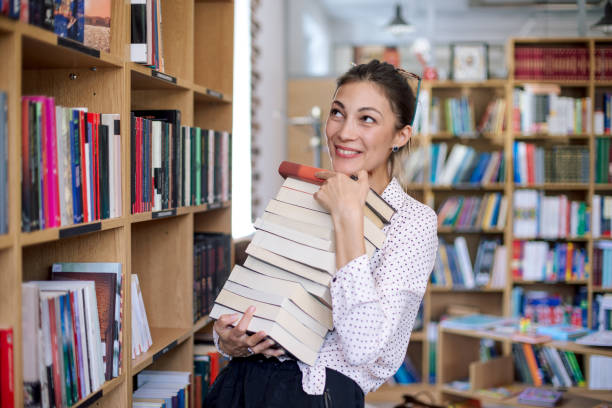 istock Happy young woman with a stack of books in library 853343980