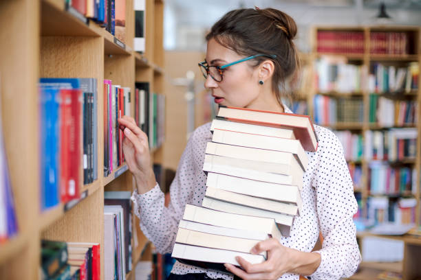 Young woman with a stack of books in library want more stock photo