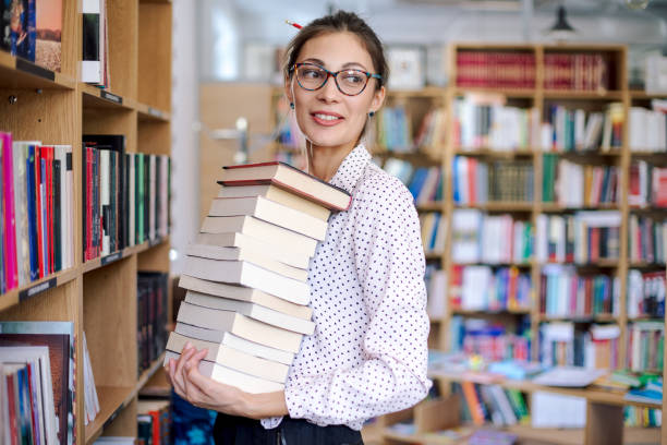 istock Young woman with a stack of books in library 853344236