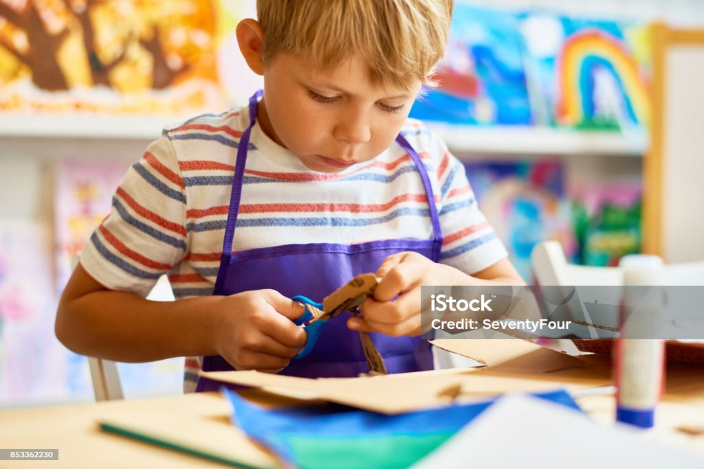 Little Boy Cutting Paper in Craft Class Portrait of cute little boy cutting paper carefully in arts and crafts class of pre-school Child Stock Photo