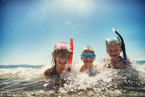 Little boys and their elder sister having fun snorkeling in beautiful sea. The boys aged 8 and girl aged 11 are laughing in warm clear water, wearing diving goggles and snorkel. Sunny summer day.\n