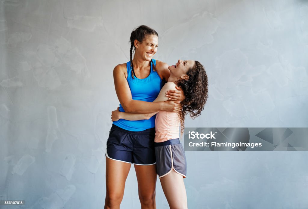 Two laughing girlfriends hugging each other after working out Two young girlfriends in sportswear standing arm in arm together in a gym laughing Gym Stock Photo