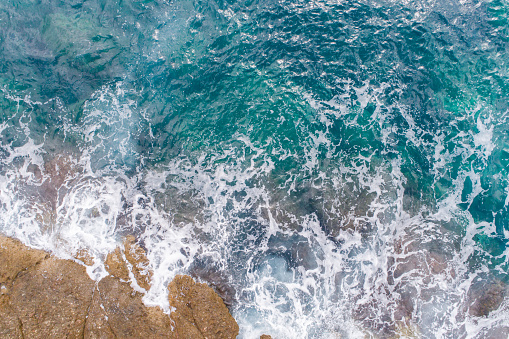 A bird's-eye view of how turquoise waves beat about sea cliffs in Montenegro